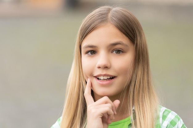 Portrait d'une adolescente heureuse souriante avec le doigt sur la joue floue à l'extérieur