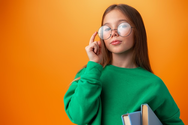 Portrait d'une adolescente intelligente avec des livres sur fond orange