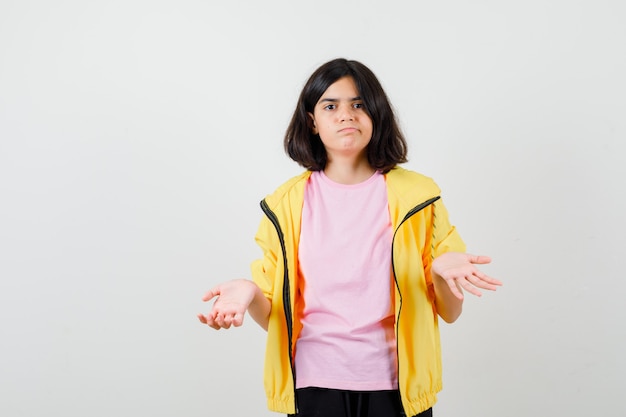 Portrait d'une adolescente montrant un geste impuissant en t-shirt, veste et regardant la vue de face pensive