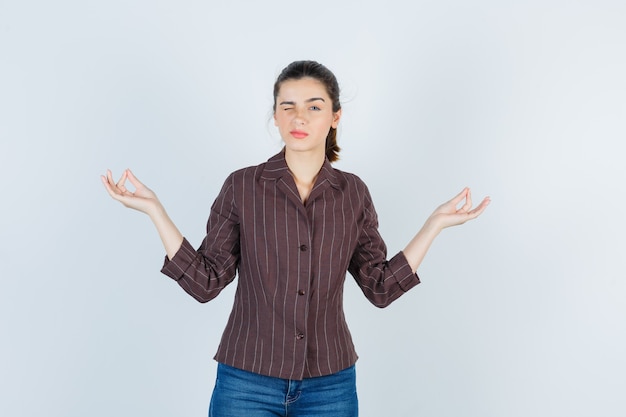 Portrait d'une adolescente montrant le geste de mudra en chemise rayée marron et regardant la vue de face pensive