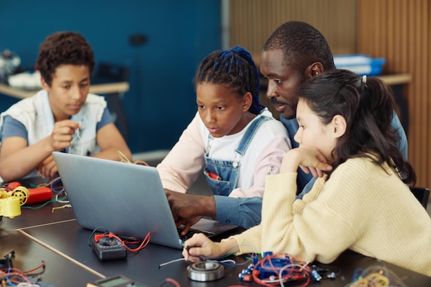 Portrait d'une adolescente noire utilisant un ordinateur portable à l'école pendant un cours d'ingénierie avec un enseignant masculin et