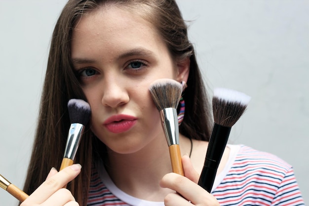 Portrait d'une adolescente avec des pinceaux pour le maquillage sur fond blanc