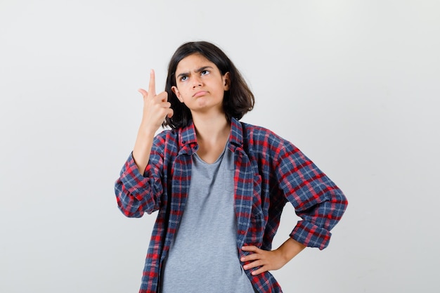 Portrait d'une adolescente pointant vers le haut, détournant les yeux, courbant les lèvres dans des vêtements décontractés et regardant la vue de face perplexe