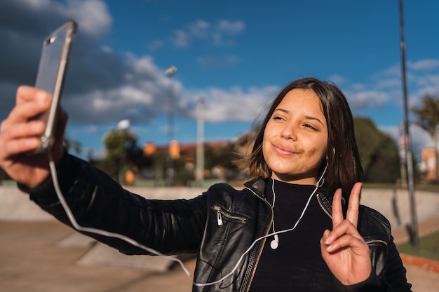 Portrait d'une adolescente prenant un selfie faisant le signe v.