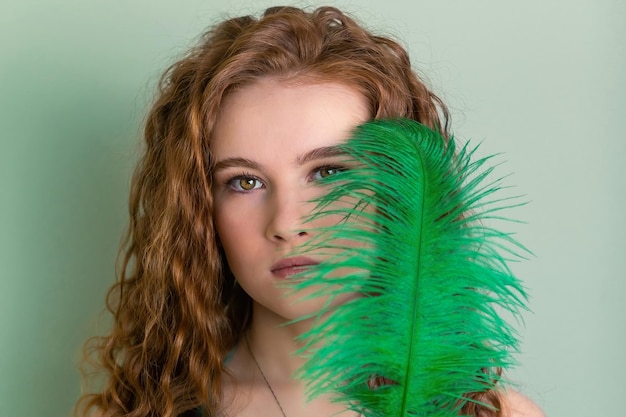 Portrait d'une adolescente rousse aux cheveux bouclés et une plume verte