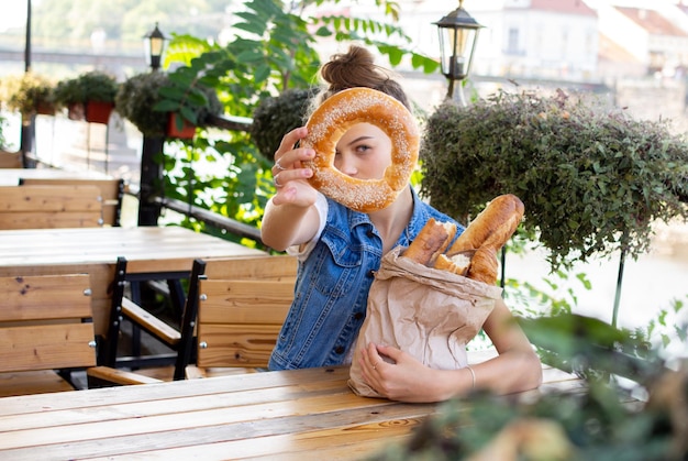 Portrait d'une adolescente avec un sac de pâtisseries fraîches qui regarde à travers un trou dans un petit pain et rit