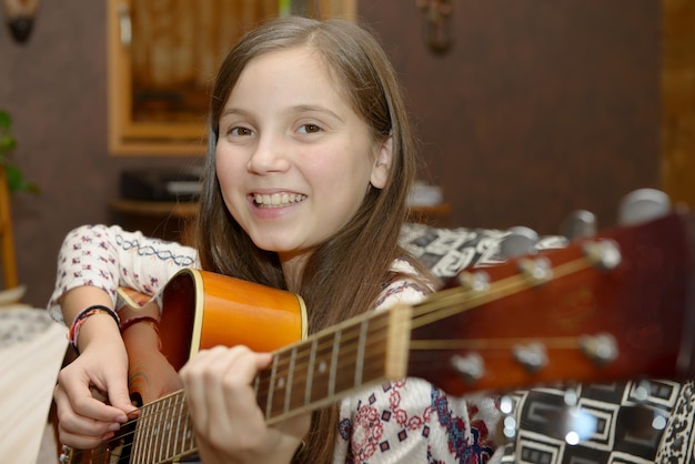 Photo portrait d'une adolescente souriante jouant de la guitare à la maison