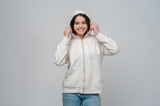 Portrait d'une adolescente souriante portant une cagoule sur la tête debout isolée sur fond gris