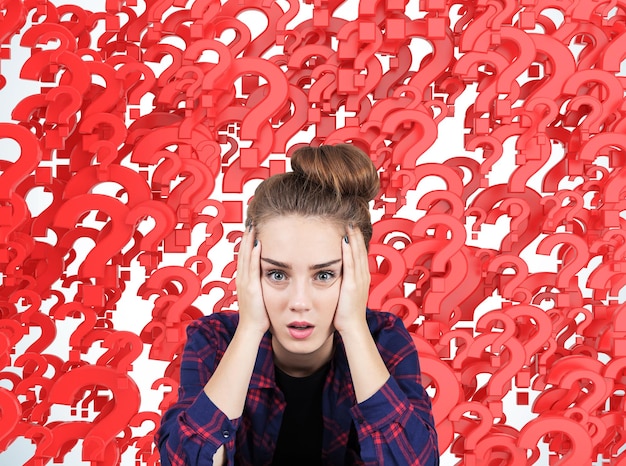 Portrait d'une adolescente stressée assise sur fond de points d'interrogation rouges. Concept de plusieurs questions auxquelles il faut répondre.