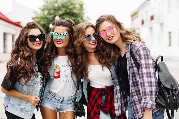 Portrait d'adolescentes heureuses dans des vêtements en denim à la mode et des lunettes de soleil marchant le long de la rue d'été avec un bel homme souriant.