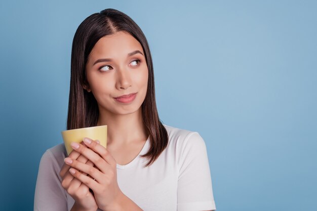 Portrait d'une adorable dame rêveuse inspirée qui tient la coupe dans un espace vide sur fond bleu