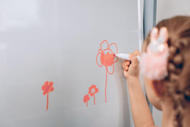 Portrait d'un adorable enfant mignon et adorable debout devant un grand tableau blanc et dessinant dessus avec un marqueur orange. Petit artiste concept.photo avec bruit
