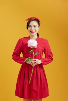 Portrait d'une adorable jeune femme debout avec un sourire charmant tenant une fleur de pivoine dans les mains et la sent
