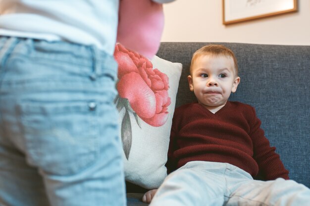 Portrait d'un adorable petit enfant en détournant les yeux pensivement assis sur le canapé à la maison, pensant avec quoi jouer.