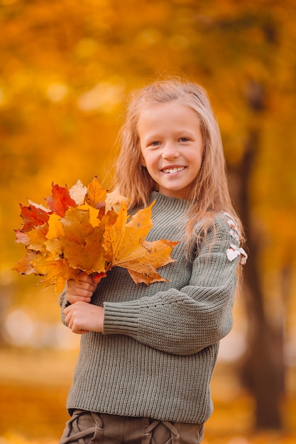 Portrait d'adorable petite fille avec bouquet de feuilles jaunes à l'automne