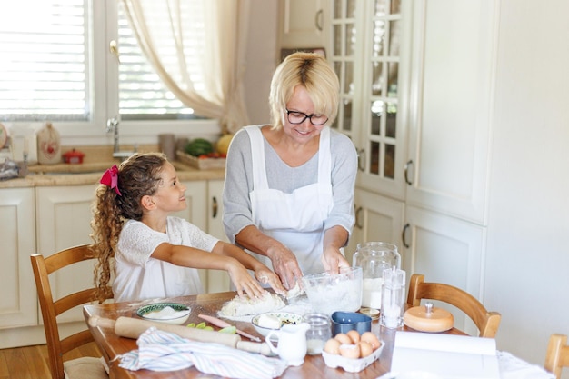 Portrait d'une adorable petite fille frisée avec sa grand-mère cuisinant ensemble à la table de la cuisine.