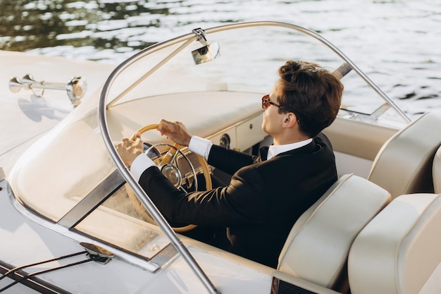 Portrait d'affaires de jeune homme en costume et lunettes de soleil posant sur un yacht