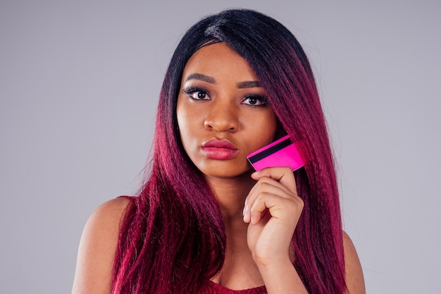 Portrait afro-américain belle femme créative coloration des cheveux teinture couleur pourpre sur fond blanc en studio coton robe tricots tenant une carte de crédit et téléphone à la main