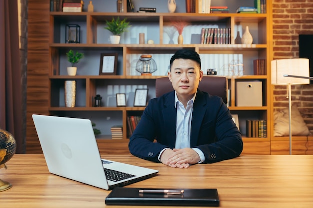 Portrait d'un agent d'assurance prospère un homme asiatique expérimenté assis à un bureau regardant la caméra le soir réussi et concentré