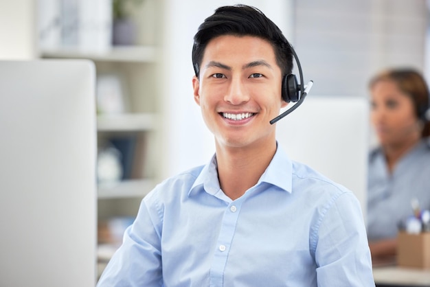 Portrait d'un agent de centre d'appels asiatique parlant au casque tout en travaillant sur un ordinateur au bureau Homme d'affaires confiant et souriant consultant et exploitant un service d'assistance pour les ventes et le service client