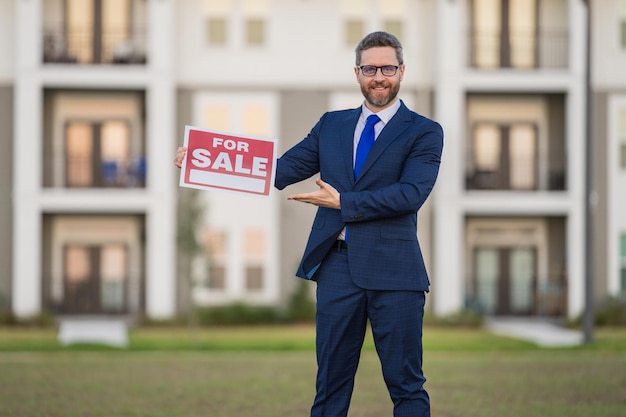 Portrait d'un agent immobilier américain debout à l'extérieur de la maison avec un tableau à vendre