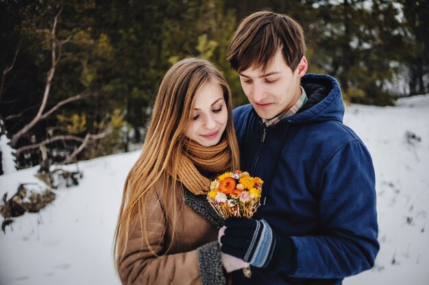 Portrait d'amoureux heureux se serrant dans ses bras à la Saint Valentin. Fille et homme tiennent dans les mains bouquet de fleurs sèches en plein air, jeune couple sensuel en hiver froid.