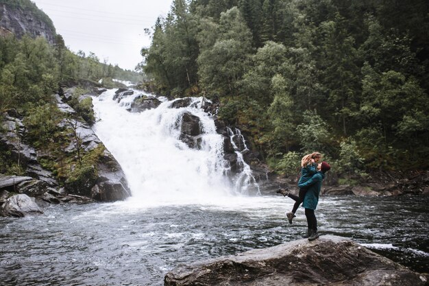 Portrait d'amoureux en imperméables verts, debout sur une pierre, contre une cascade