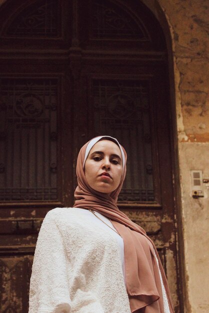 Portrait à angle bas d'une jeune femme portant un hijab debout contre la porte