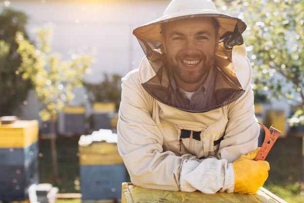 Portrait d'un apiculteur mâle heureux travaillant dans un rucher près de ruches avec des abeilles Recueillir du miel Apiculteur sur le rucher Concept d'apiculture