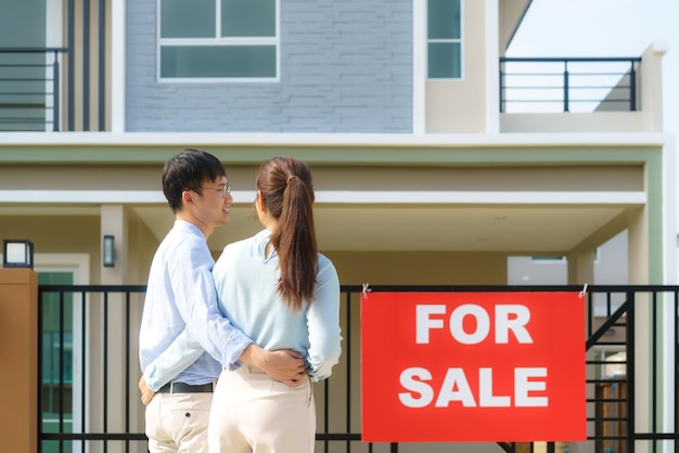 Portrait arrière d'un jeune couple asiatique debout et serrant ensemble l'air heureux devant leur nouvelle maison pour commencer une nouvelle vie. Concept de famille, d'âge, de maison, d'immobilier et de personnes.