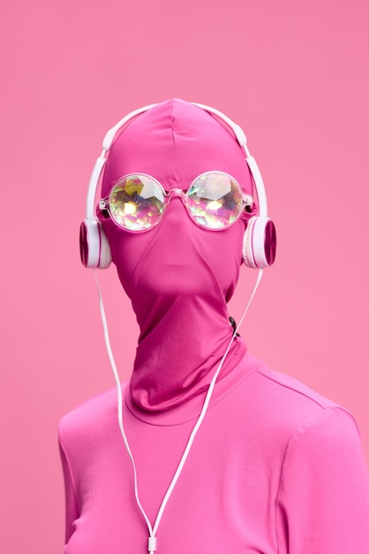 Portrait d'art d'une femme portant un masque de cambrioleur rose avec des lunettes rondes brillantes portant des vêtements roses avec des écouteurs roses sur un fond rose regardant dans la caméra Photo de haute qualité