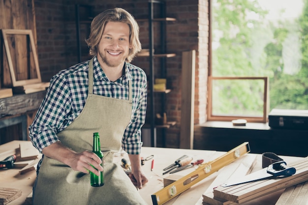 Portrait d'artisan barbu posant dans sa menuiserie tenant une bière