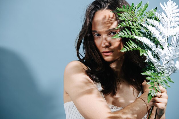 Portrait artistique d'une belle brune vitiligo assise avec une branche de fougère