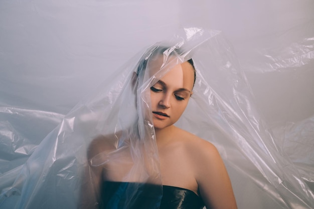 Portrait artistique. Pollution plastique. Problème d'écologie. Réduction du gaspillage. Femme pensive déçue fatiguée dans un sac en film de polyéthylène transparent isolé sur fond d'espace de copie clair.