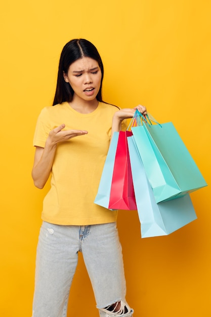 Portrait asiatique belle jeune femme dans un t-shirt jaune avec des sacs à provisions multicolores modèle de studio inchangé