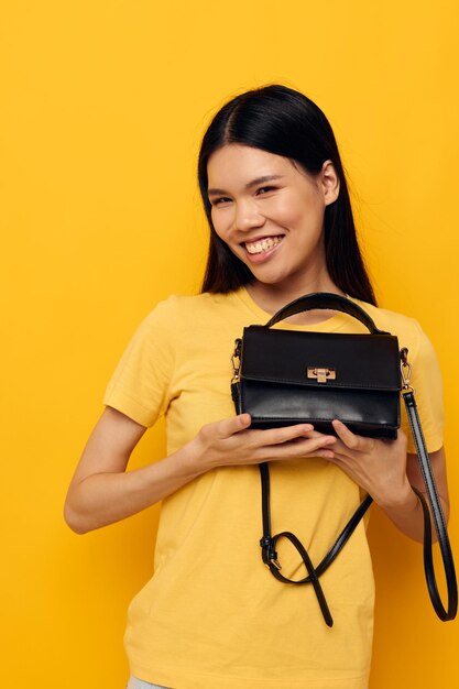 Portrait asiatique belle jeune femme avec un sac de femme noire dans ses mains fond jaune inchangé