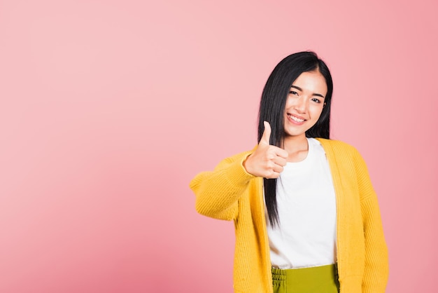 Portrait asiatique belle jeune femme sourire elle debout fait doigt pouce vers le haut, signe Ok pour accepter studio tourné isolé sur fond rose, femme thaïlandaise réussie comme geste du doigt avec espace de copie