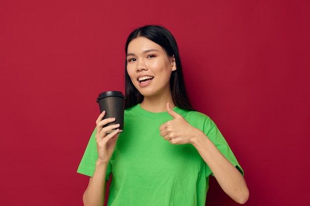 Portrait asiatique belle jeune femme sourire vert tshirt noir gobelets jetables mode fond rouge inchangé