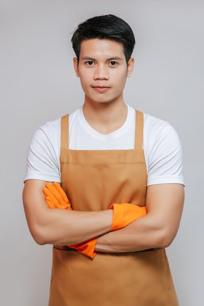 Portrait asiatique jeune beau mand stand avec les bras croisés, il porte un tablier et des gants en caoutchouc, sourit et regarde vers la caméra, espace de copie