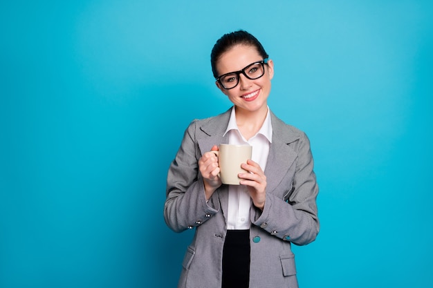 Portrait de l'assistant du chef de la direction positif tenir latte aromatique porter une veste de blazer de costume gris isolé sur fond de couleur bleu
