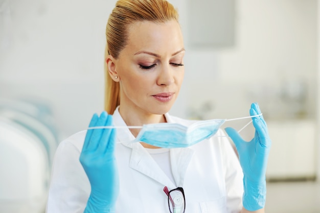 Portrait d'assistant de laboratoire blond attrayant avec des gants en caoutchouc debout à l'hôpital et mettre un masque stérile.