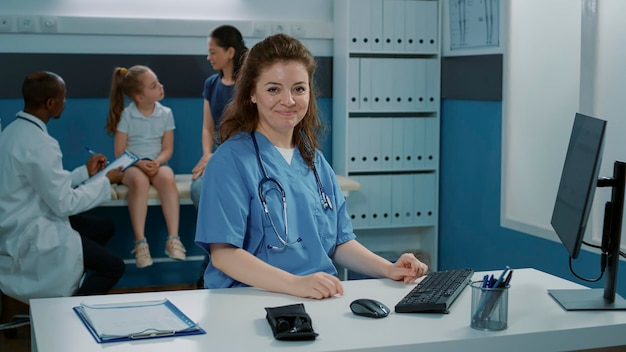 Portrait d'un assistant médical travaillant sur le service de rendez-vous, utilisant un ordinateur au bureau. Infirmière en uniforme assise au bureau, se préparant à apporter son aide lors de la visite de contrôle.