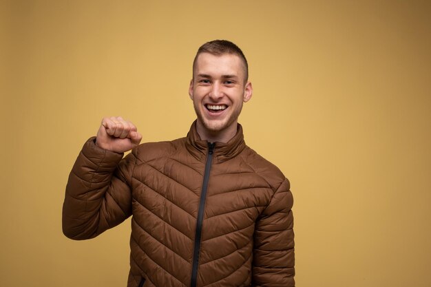 Portrait d'atelier. Jeune homme des années 20 dans une veste marron, sur fond jaune, démontrant les muscles du biceps sur ses bras, démontrant le pouvoir de la force