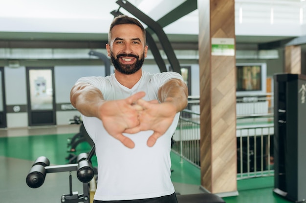 Portrait d'un athlète dans la salle de gym Un homme portant un t-shirt blanc sourit et fait des exercices