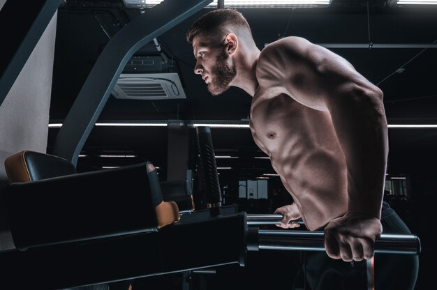 Portrait d'un athlète faisant des pompes sur les barres asymétriques de la salle de sport. Concept de musculation et de remise en forme. Technique mixte