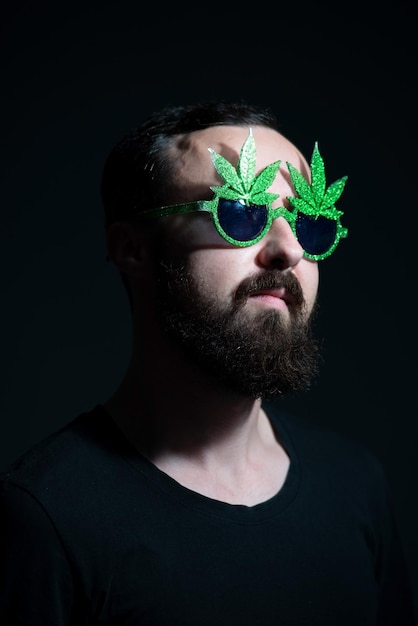 Portrait authentique d'un mec joyeux en lunettes de soleil marijuana sur fond sombre