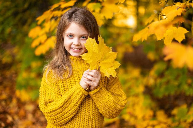 Portrait d'automne heureux enfant souriant tenant dans les mains des feuilles d'érable jaune en arrière-plan d'automne