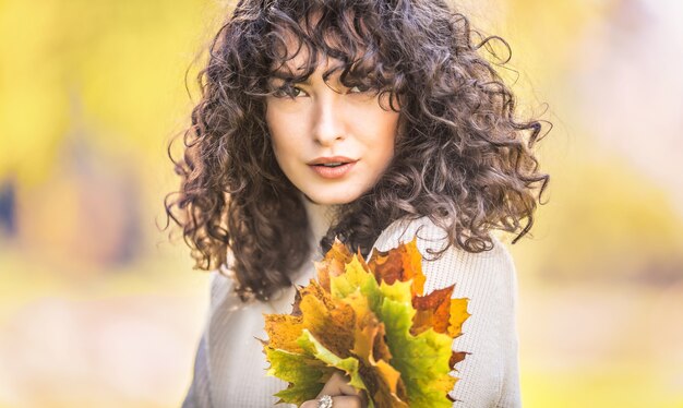 Portrait d'automne de jeune femme aux cheveux bouclés et bouquet de feuilles d'érable.