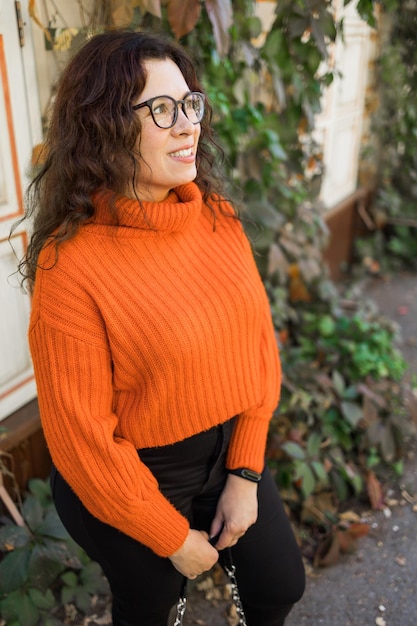 Photo portrait d'automne d'une jolie jeune femme à lunettes élégantes dans un pull orange à la mode tricoté sur fond de feuilles fille se promène dans la ville