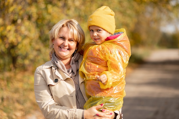 Portrait d'automne de la mère et de la petite fille vêtue d'un chapeau jaune, maman tenant une fille dans ses bras parmi les feuilles jaunes